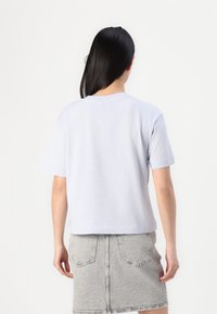 Lichtpaarse casual t-shirt met korte mouwen en een ronde halslijn, gecombineerd met een grijze denim rok, gezien vanuit de achterkant.