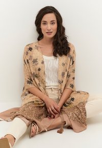 Beige ja pruuni lillemustriga kimono tekstuursete kangaste ja narmastega äärel, kihtidena kerge kudumisega topi ja koorevärvi pükste peal.