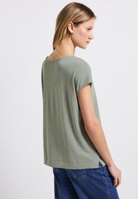 Krátký rukáv, světle zelený top z hladké látky s volným střihem, s kulatým výstřihem a rozparky na okrajích.