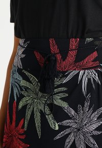 Blommig kjol med svart bakgrund och flerfärgade palmlovs mönster i grönt, rött och vitt. Inkluderar en knytdetalj med tofs.