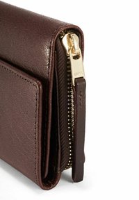 Zbliżenie rogu ciemnobrązowego skórzanego portfela z złotym zamkiem błyskawicznym i skórzaną pętelką na zamku na białym tle.