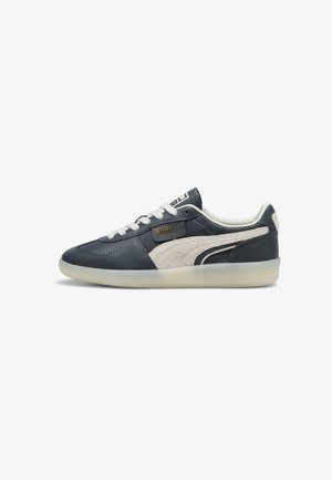 Navy mėlynos odinės sportbačiai su smėlio spalvos zomšos akcentais, perforuota struktūra, balti raišteliai ir permatomas guminis padas. Yra Puma logotipo detalės.