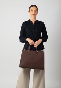 Brown leather tote bag with textured surface, rectangular shape, two rounded handles, and gold-tone hardware accents.