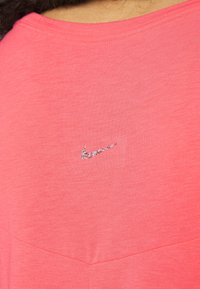 camiseta de Nike en coral brillante, con una textura suave, cuello redondo y un pequeño logo brillante en el pecho. Diseño simple y casual.