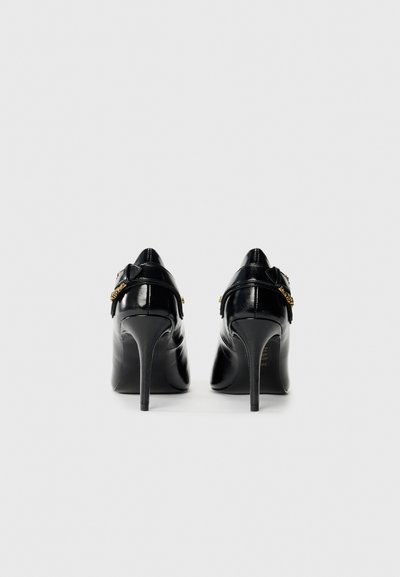 Escarpins noirs en cuir verni à talons hauts avec un bout pointu, dotés d'une sangle et d'une boucle dorée sur le talon. Texture lisse.