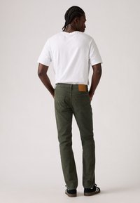 Pantaloni in cotone verde oliva con taglio slim e tasche posteriori. T-shirt bianca, seduta con capelli intrecciati, che mette in mostra uno stile casual.