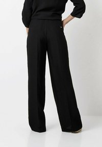 Black, wide-leg pants with a crinkled texture, featuring back pockets and subtle metallic accent. Made from lightweight fabric.