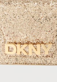 Χρυσό γκλίτερ clutch DKNY με υφή στην επιφάνεια, με έντονο χρυσό λογότυπο. Συμπαγής ορθογώνιο σχήμα, λαμπερά στοιχεία σε όλη την επιφάνεια.