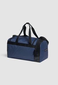 Bolsa de viaje de la marina hecha de nylon duradero. Cuenta con correas negras, bolsillo lateral de malla, cierre con cremallera y una base plana para mayor estabilidad.