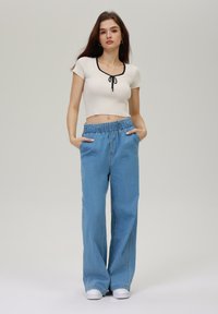 Hvit ribbet croptopp med svart nakkedetalj, kombinert med lyseblå bredbein denim bukser med elastisk liv og sidelommer.