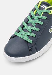Marineblauwe leren sneakers met groene veters, witte rubberen zool en geborduurd logo. Soepele textuur en klassiek ontwerp.