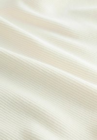 Nahaufnahme eines weichen Creme-Stoffs mit feiner horizontaler Rippstruktur und sanften Falten.