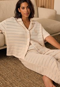 Beige Strick-Loungewear-Set, bestehend aus einem kurzärmeligen, knöpfbaren Oberteil mit Streifen und passenden Hosen mit einer softweichen Textur.