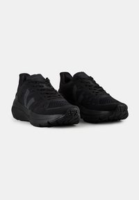 Černé atletické boty s prodyšným síťovaným svrškem, texturovanou gumovou podrážkou a polstrovaným jazykem. Má minimální branding a šněrování.