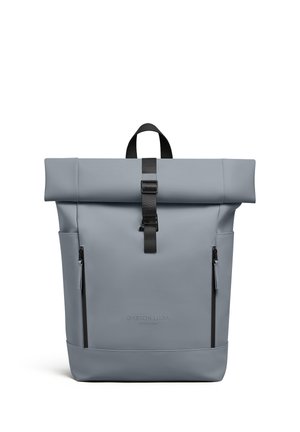 Lichtgrijze roll-top rugzak met zwarte gesp, twee verticale ritssluitingen en het Gaston Luga Stockholm-logo aan de voorkant.