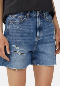 Shorts en denim bleu clair, présentant des déchirures usées, un ourlet effiloché, un design classique à 5 poches et un système de bouton à la taille.