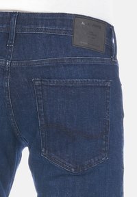 Vaqueros de mezclilla azul oscuro con un corte recto, que presentan un bolsillo trasero y un parche de cuero de la marca cerca de la cinturilla. Tela texturizada.