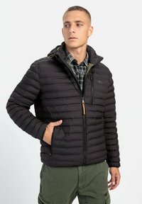 Sort dunjakke med lynlås foran, vandret quiltet design, justerbar hætte og forlommer; båret over en ternet skjorte.