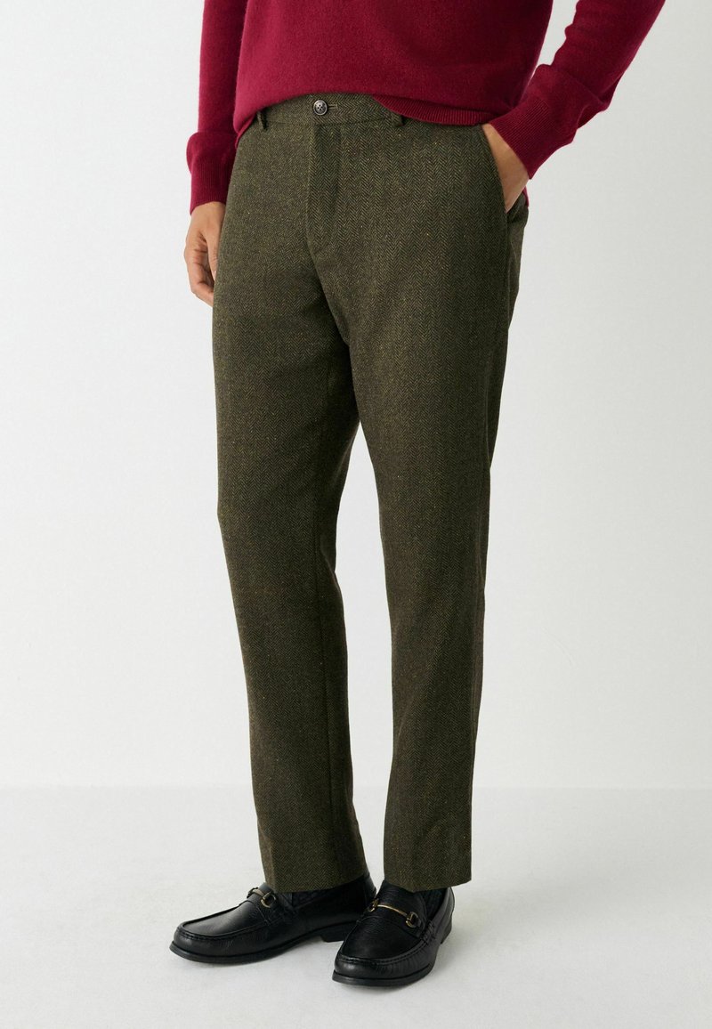 Olivgröna herringbone-byxor med rak passform, knäppning och sidofickor, kombinerat med svarta loafers och en vinröd tröja.