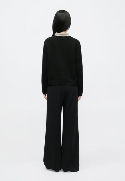 Μαύρο φαρδύ πουλόβερ με μπεζ γιακά, υφή πλεκτού, ριμπ τελείωμα και μανσέτες. Συνδυασμένο με μαύρο παντελόνι φαρδιάς γραμμής, μίνιμαλ σχεδιασμός.