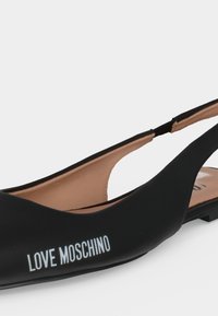 Μαύρο φλατ παπούτσι slingback με "Love Moschino" τυπωμένο λευκό στο πλάι και μπεζ εσωτερική επένδυση.