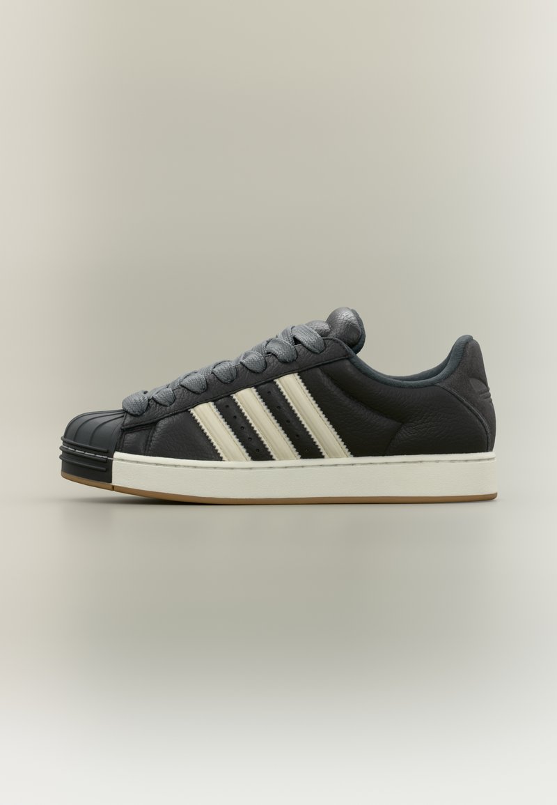 Juodos odos sportinis batelis su balta padu, trimis baltais šonais dryžiais, pilkomis raištelėmis ir juodu guminiu priekine dalimi.