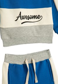 Blauwe en grijze trainingspak met een gestreept ontwerp en de tekst "Awesome", geribbelde manchetten en een elastische tailleband met trekkoorden.