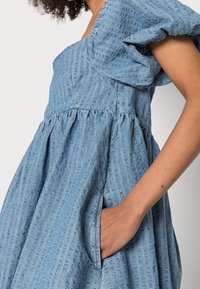 Blå denimklänning med puffärmar, texturerad tyg med vertikala ränder, rynkad midja och sidofickor.