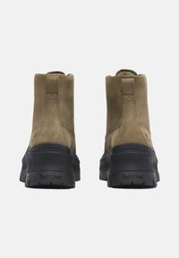 Brown suede ankle boots with a black rubber sole. Features minimal stitching and a logo on the heel. Smooth texture with a slightly glossy finish.