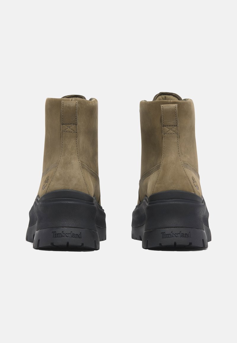 Braune Wildleder-Ankelboots mit einer schwarzen Gummisohle. Minimalistische Nähte und ein Logo an der Ferse. Glatte Textur mit einem leicht glänzenden Finish.