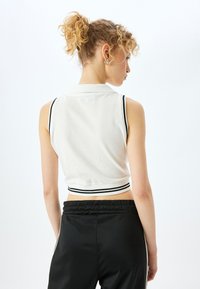 Witte, cropped polo met zwarte rand, voorzien van een kraag en zonder mouwen, gecombineerd met zwarte sportieve broeken. Glad van textuur.