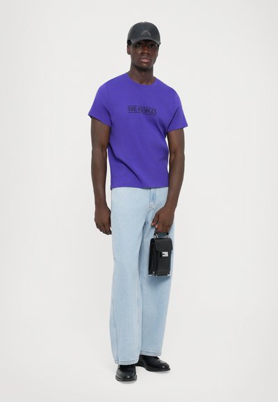 Μωβ βαμβακερό T-shirt με κοντά μανίκια και μαύρο κείμενο; ανοιχτό μπλε φαρδιά τζιν παντελόνι; μαύρη τσάντα με ασημένια υλικά; μαύρα παπούτσια.