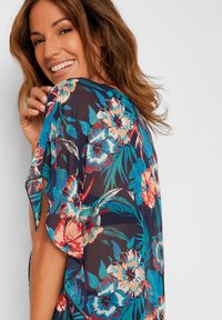 Kimono floreale in tessuto leggero e trasparente, con vivaci fiori blu, rossi e bianchi su uno sfondo navy scuro, dotato di aperture laterali.