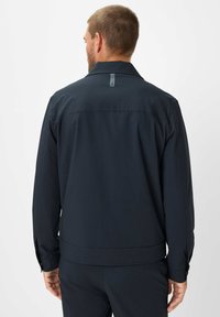 Marineblauwe jas met een kraag, zichtbare stiksels en een rechte snit. Voorzien van een klein label aan de achterkant van de halslijn en knoopmanchetten.
