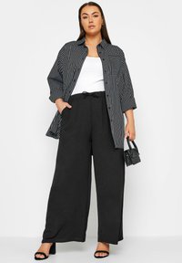 Mustavalkoraitainen ylisuuria paita, valkoinen toppi, löysät mustat housut ja mustat korkeakorkoiset sandaalit; pitäen pientä mustaa käsilaukkua.