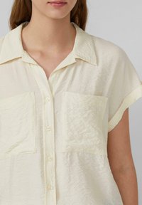 Lichtgele, gekreukelde stoffen shirt met een kraag, korte mouwen en twee voorzakken met knoopsluitingen.
