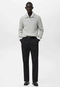 Maglione a coste grigio chiaro con colletto abbinato a pantaloni sartoriali neri. Le scarpe sono nere lucide con finitura liscia.