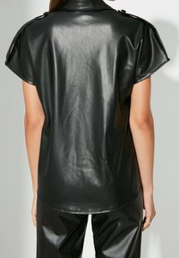 Top corto a maniche corte in faux leather nero con colletto strutturato e dettagli con bottoni, caratterizzato da una texture liscia e lucida e una silhouette aderente.