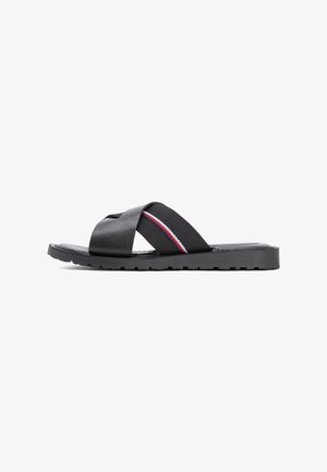 Black slide sandal with a thick rubber sole and crossed straps, one with a red, white, and blue stripe detail on a white background.