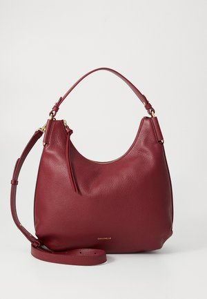 Hobo bag in deep red pebbled leather, featuring a gold zipper, adjustable shoulder strap, and subtle logo accent at the base.