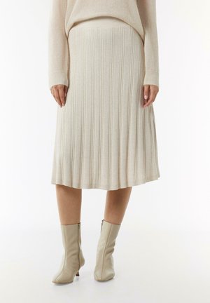 Strickrock in Creme mit plissierter Silhouette und geripptem Textur. Kombiniert mit beigen Knöchelstiefeln mit seitlichem Reißverschluss.