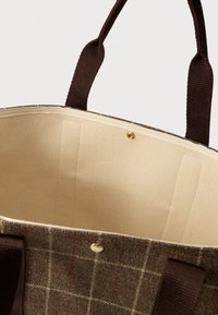 Τσάντα φάκελος με καφέ καρό εξωτερικό, μπεζ ύφασμα εσωτερικά, σκούρους καφέ χειρολαβές και χρυσό κουμπί κούμπωμα σε λευκό φόντο.