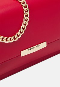 Czerwona skórzana torebka na ramię z złotym łańcuchem i złotą tabliczką z nazwą marki. Gładka tekstura z precyzyjnymi szwami i akcentami.