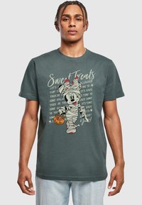 Mörkgrå t-shirt med en tecknad karaktär insvept i bandage, som h�åller en orange pumpa-bucket, med text i krämfärg.