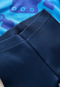 Blå stof med et dristigt, mørkt mønster, der har runde former. Mørkeblå ribbede leggings med elastisk talje og glat tekstur.
