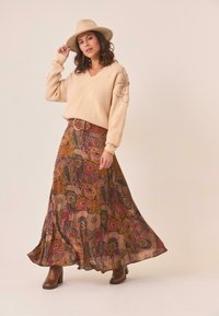 Suéter de punto beige con escote en V y detalles florales, combinado con una falda larga y fluida de patrón multicolor y botas de tacón marrones.