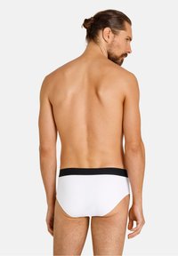 Weiße Unterhose mit einem schwarzen Elastikbund, von hinten gezeigt. Glatte Stofftextur, minimalistisches Design und figurnaher Schnitt.