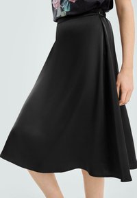 Czarna spódnica w kształcie litery A wykonana z gładkiego materiału, charakteryzująca się subtelnym połyskiem i zwiewnym krojem. Pas spódnicy usytuowany jest na naturalnej linii talii.
