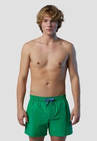 Costumi da bagno verdi realizzati in tessuto leggero, con vita elasticizzata, cordino viola e una vestibilità rilassata.