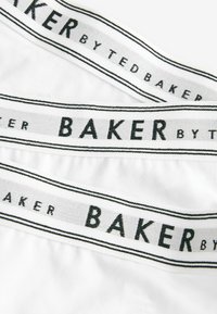 Sous-vêtements en coton blanc avec une ceinture élastique rayée noire portant le texte "BAKER BY TED BAKER" en lettres majuscules.